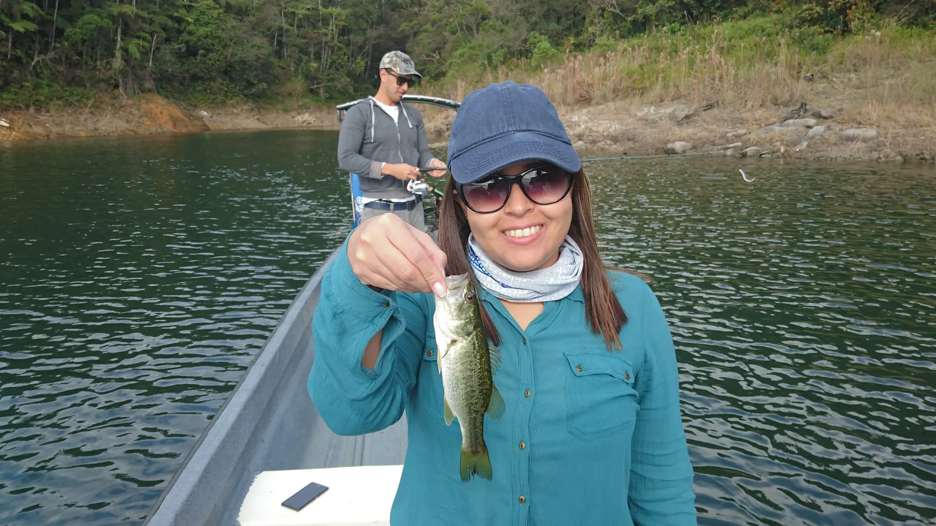Juliana sostiene con emoción su primera mojarra capturada, sonriendo junto al bote.