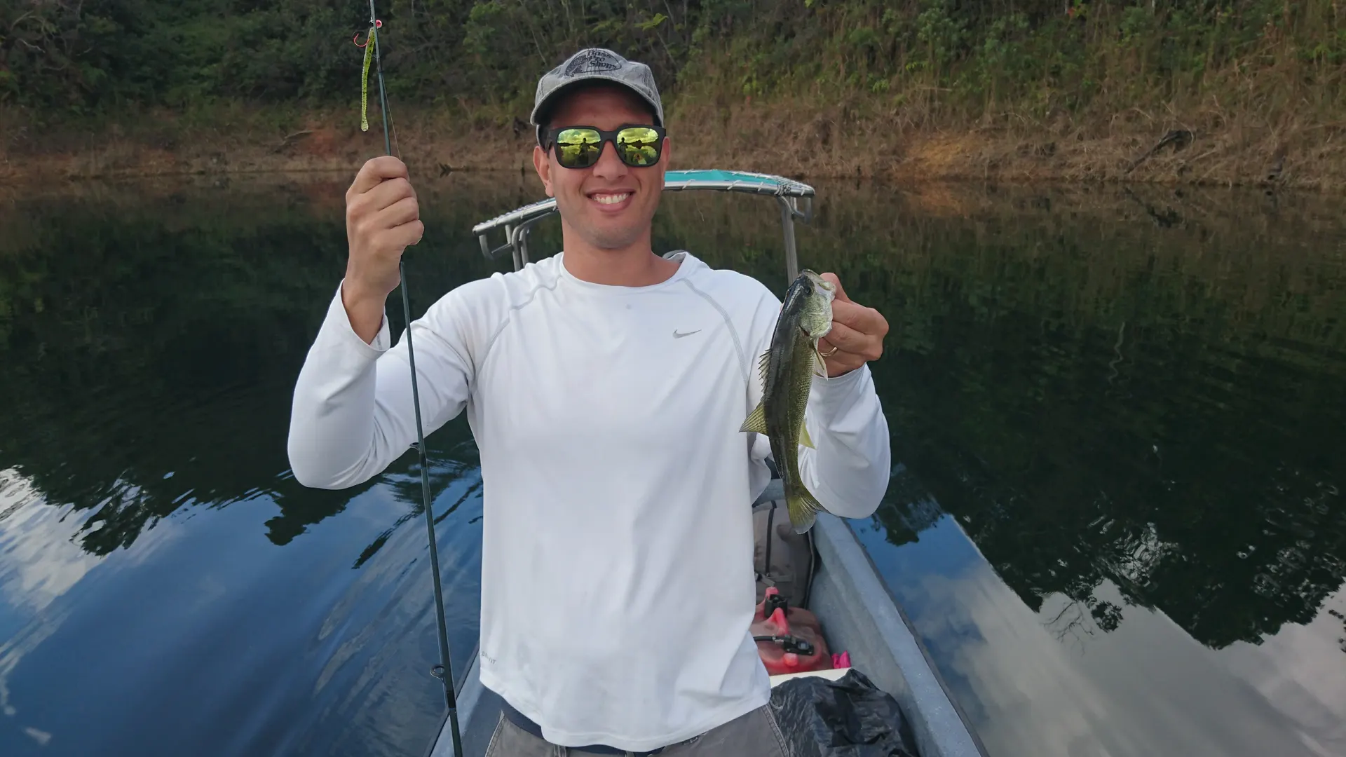 Pedro sostiene un black bass recién capturado con un gusano de plástico blanco.