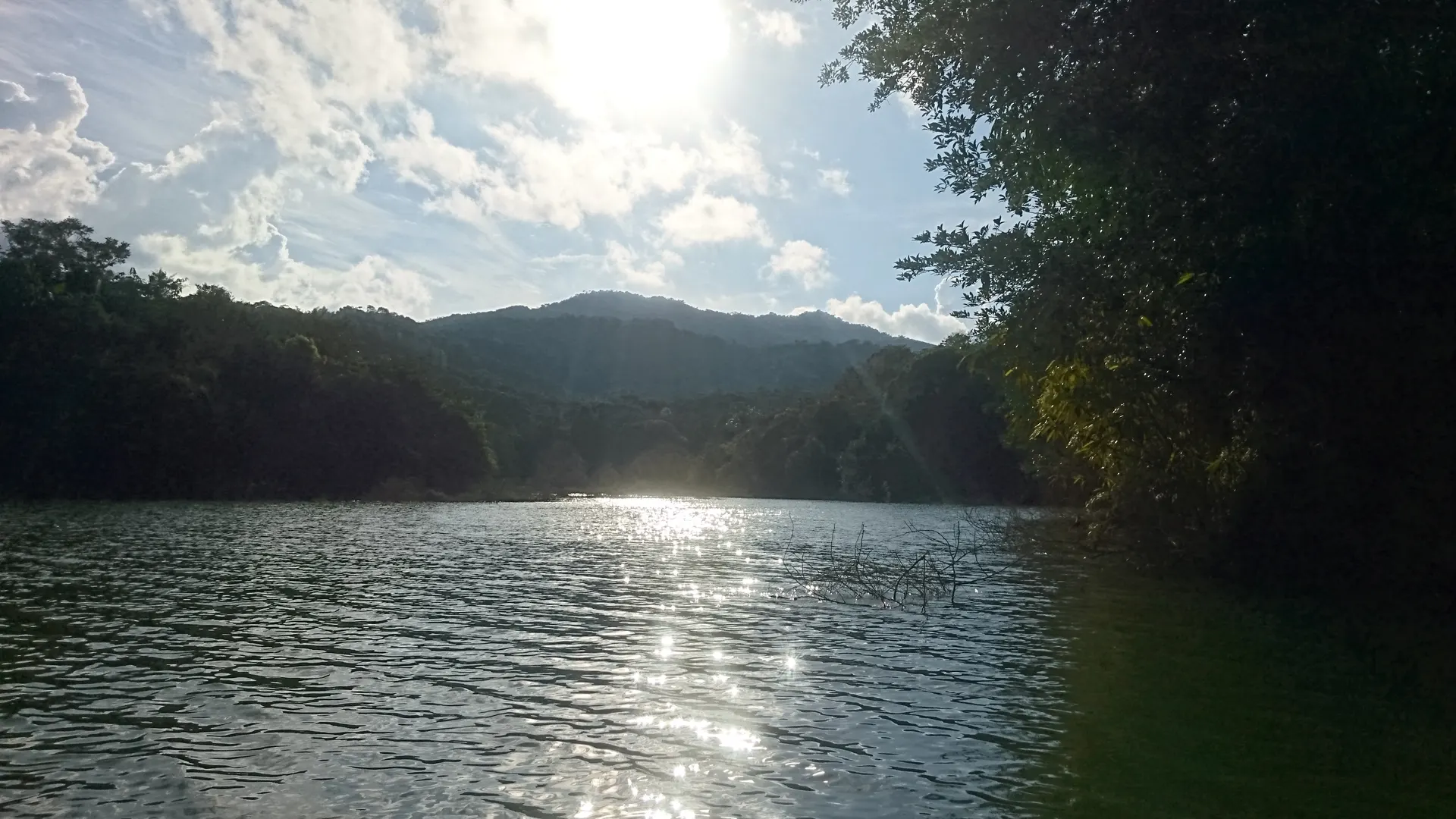 Un embalse a contraluz al final de la tarde, con el sol reflejándose en el agua y las montañas en silueta.