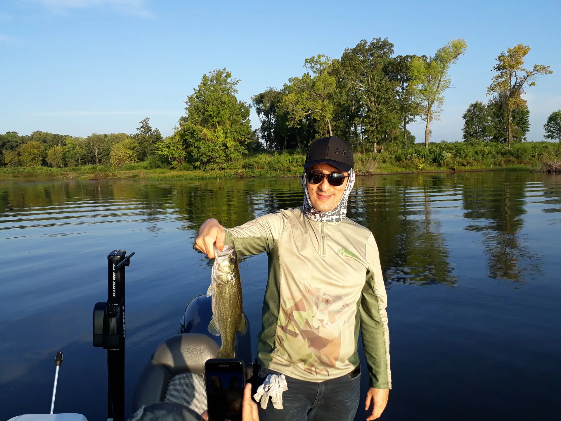 Un black bass es sostenido con una mano mostrando su cuerpo oscuro moteado.
