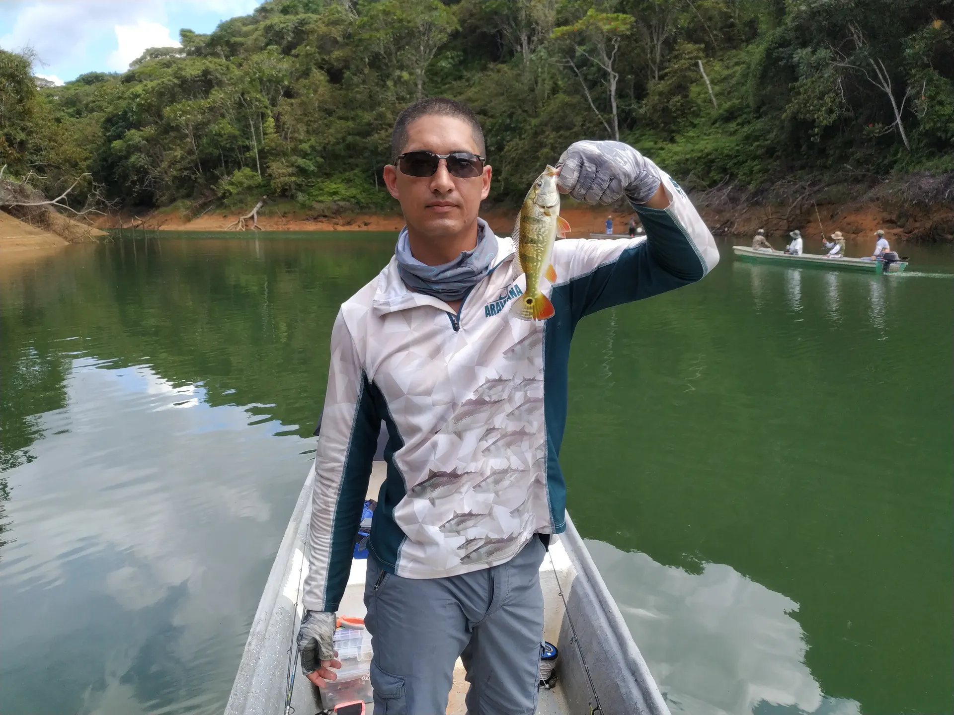 Un tucunare de manchas oscuras es sostenido con una mano sobre el bote.