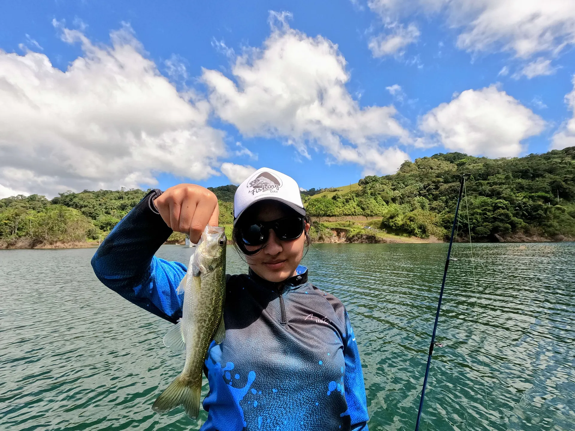 Valeria sostiene un black bass pequeño recién capturado en la mañana sobre el bote.