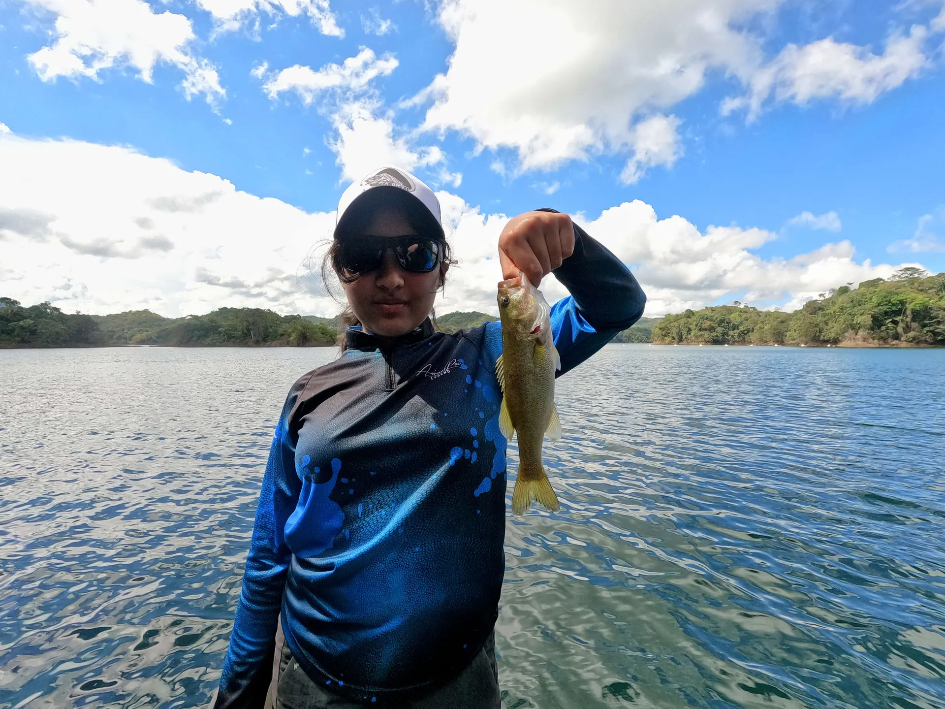 Un black bass es levantado del agua mostrando su cuerpo oscuro moteado.