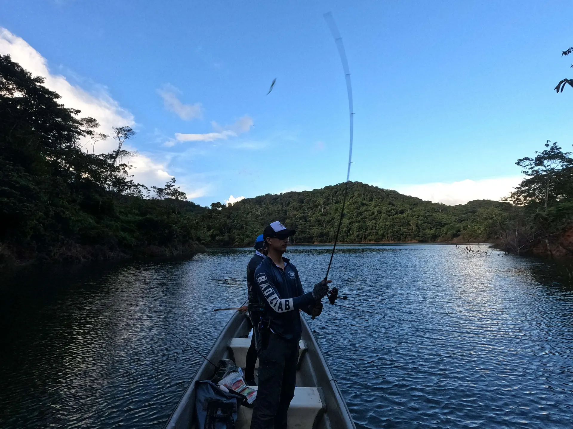El embalse de Jaguas en calma con montañas de selva reflejadas en el agua bajo un cielo nublado.