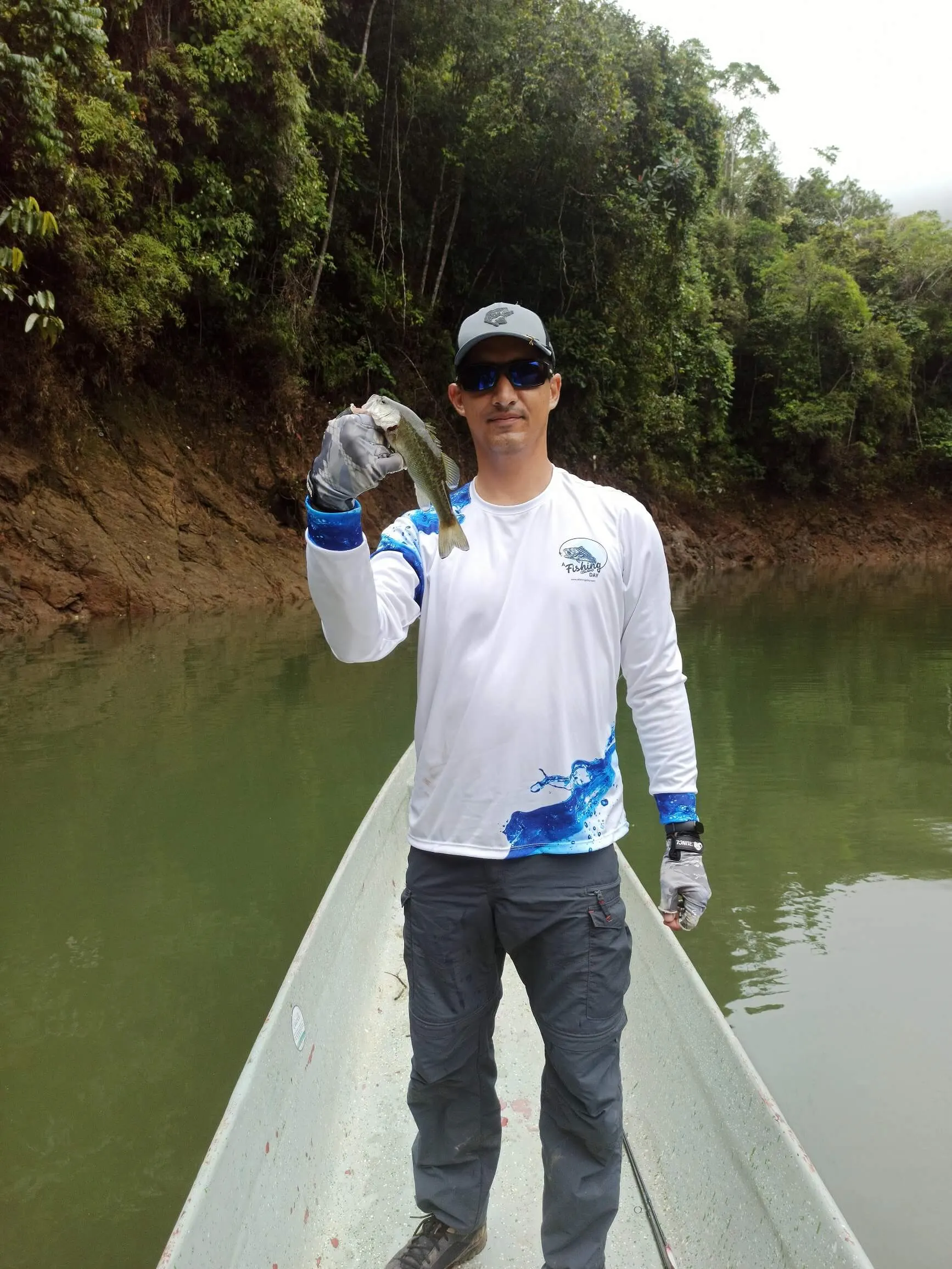 Una joven pescadora sonríe sosteniendo un black bass pequeño con ambas manos en el bote.