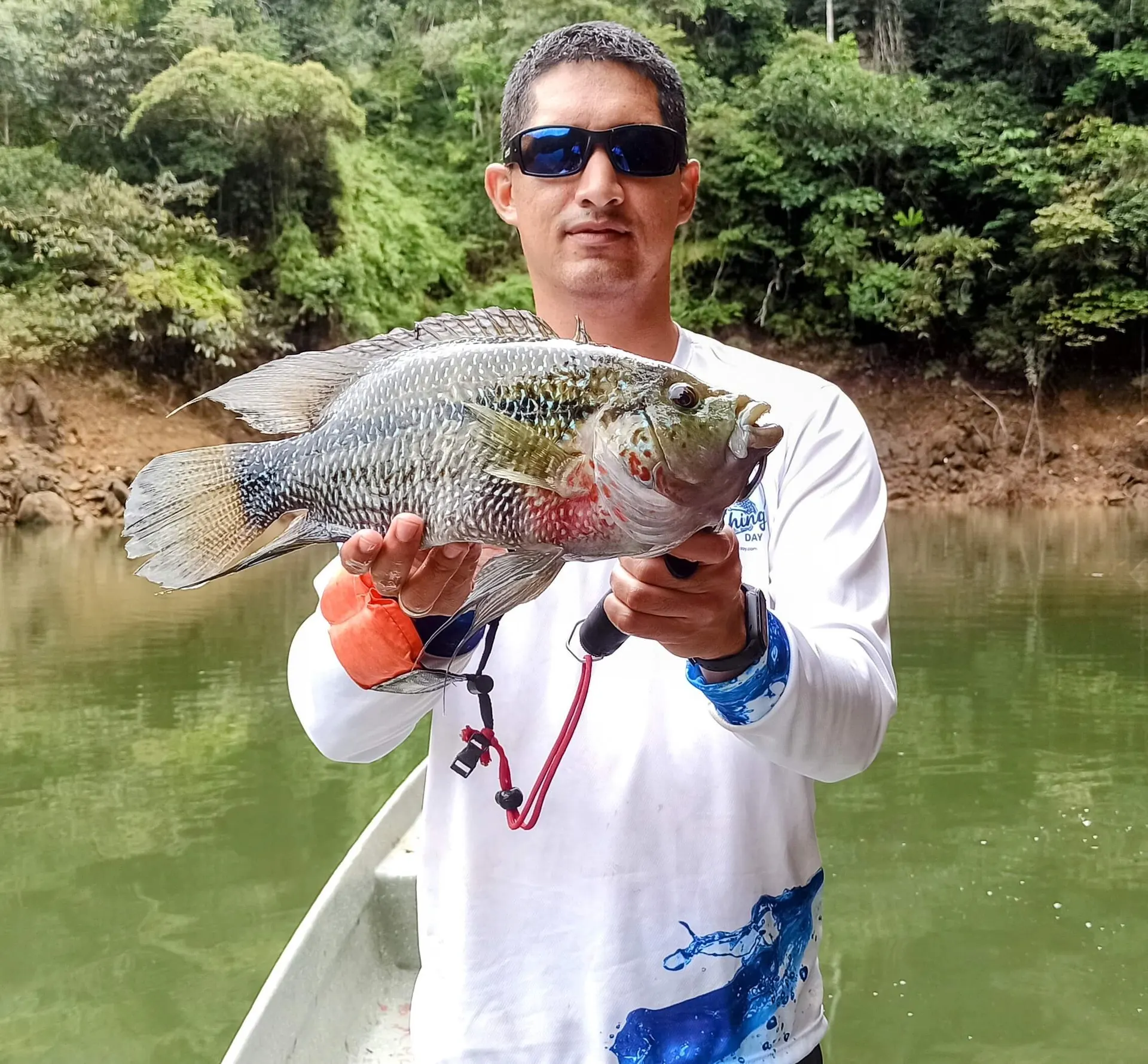 Una mojarra de unos 40 centímetros es levantada con orgullo, mostrando su cuerpo plateado y aletas oscuras.