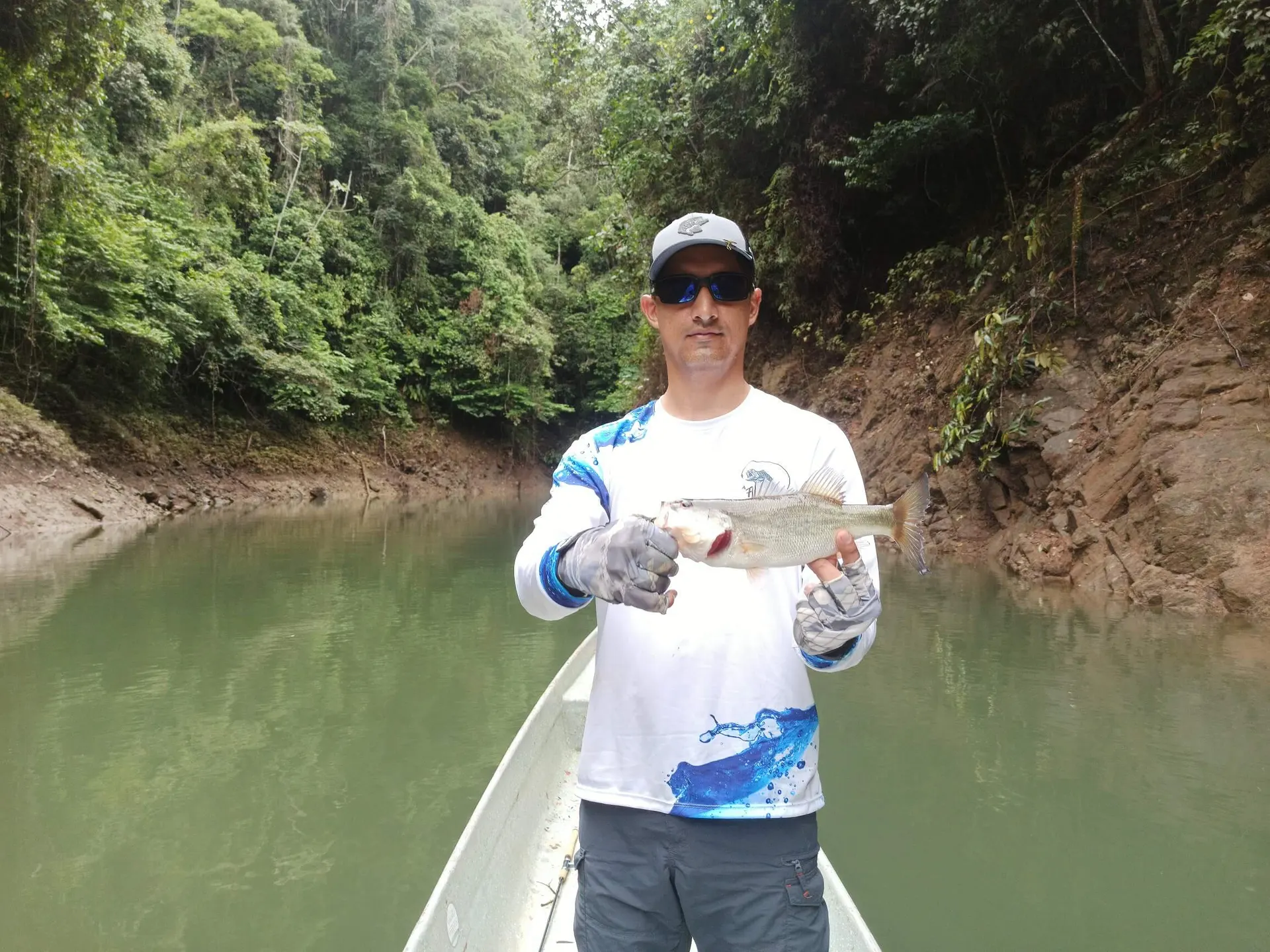 Una mojarra de escamas plateadas es levantada del anzuelo sobre el agua del embalse de Punchina.