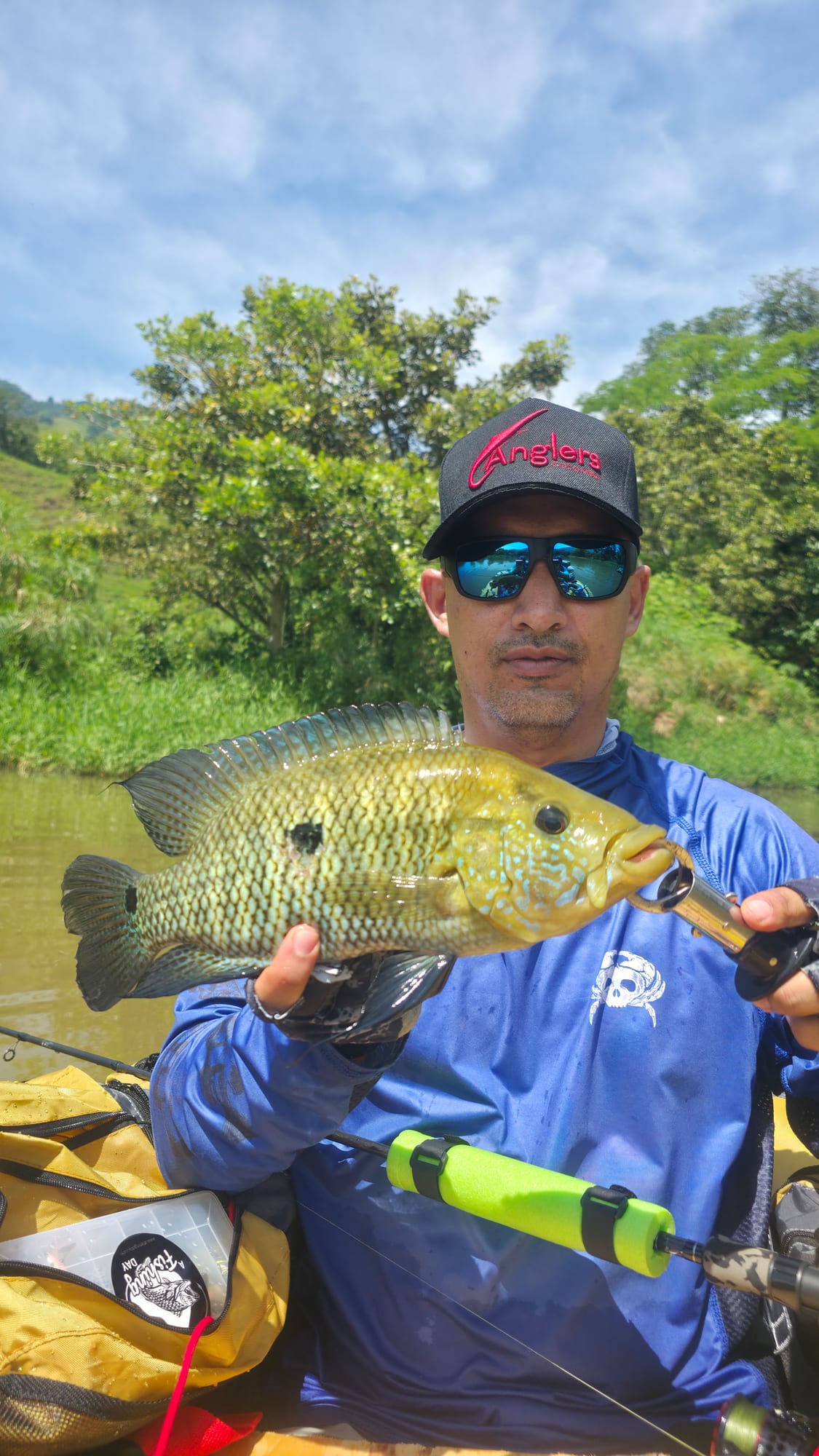 Pescador en un belly boat amarillo sosteniendo una mojarra capturada en los lagos de La Frisolera.
